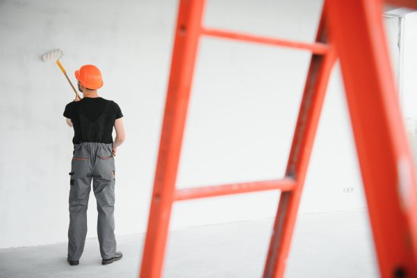 Building contractor painting grey wall with roller brush.