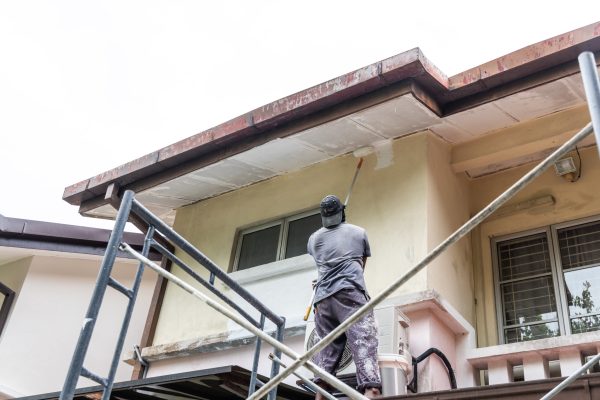 Painter worker adding undercoat foundation paint onto ceiling as primer with roller at residential building.